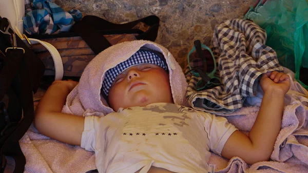 Kumsalda, gölgede, başında havluyla uyuyan tatlı bir çocuk. Mutlu çocuklar dinleniyor