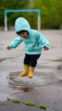 Kapüşonlu küçük bir çocuğun portresi yağmurdan sonra baharda su birikintisine atlıyor.