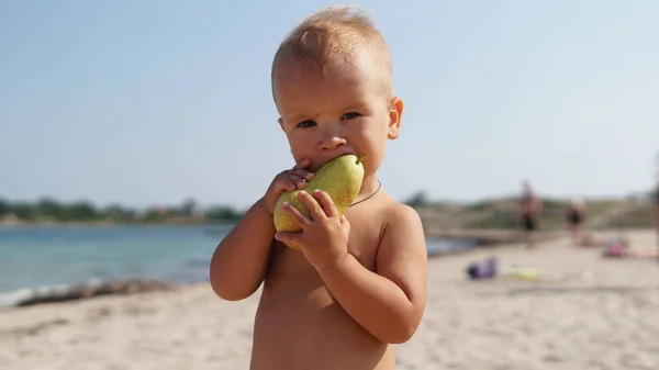 Słodkie Dziecko Stojące Plaży Jedzące Smaczną Gruszkę Patrzące Aparat Bardzo — Zdjęcie stockowe