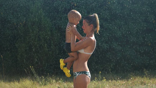 Joven Madre Parada Bajo Rocío Del Agua Sosteniendo Pequeño Hijo —  Fotos de Stock