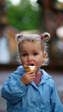 Mavi ceketli, yaz parkında dondurma yiyen küçük bir kız. Yüzüne dondurma bulaştırdım.
