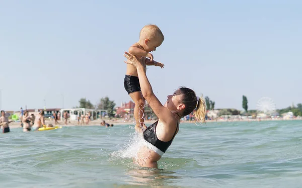 若いですお母さん立って水で海とスローアップ笑顔小さな笑顔息子で彼女の腕 — ストック写真