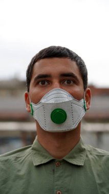 Dışarıda yeşil kapakçığı olan koruyucu maskeli genç bir adamın portresi. Salgın ve koronavirüs karantinasında sağlık ve güvenlik kavramı
