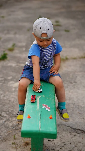 一个戴帽子的可爱小男孩在操场上玩玩具车 — 图库照片