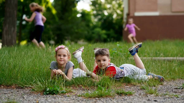 小模特儿们可爱的女孩和男孩一起躺在草坪上的草地上 看着相机 第一个童年关系 — 图库照片