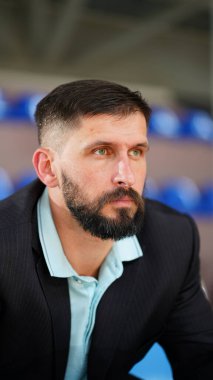 Basketbol sahasında spor ceketli genç bir adam. Basketbol koçu takımının maçını izliyor.