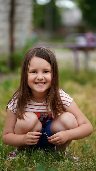 長い髪を持つかわいい女の子の肖像画草の上にスクワットし 夏に屋外で笑顔 — ストック写真