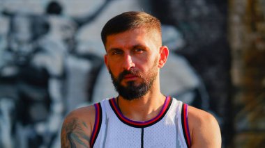 Jersey 'de sakallı bir basketbolcu basketbol arka planına bakıyor.