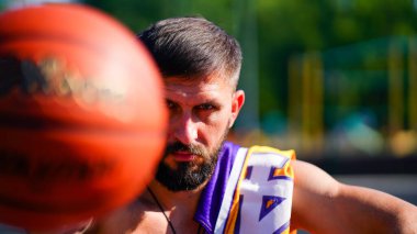 Sakalsız, sakalsız, omuzunda forması olan basketbol sahasında oturan ve topu eliyle tutan yetenekli bir atlet.