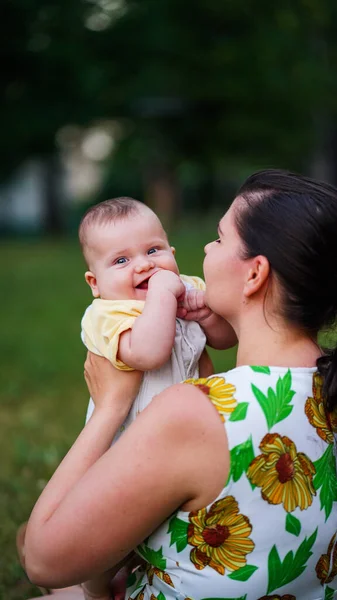 Little baby on arms of mother bite his own hand and smiling at same time outdoors