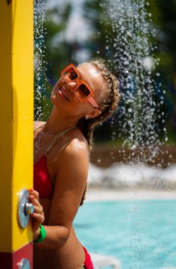 Saçları örgülü güzel bir kadın su parkında akan suyun altında duruyor..