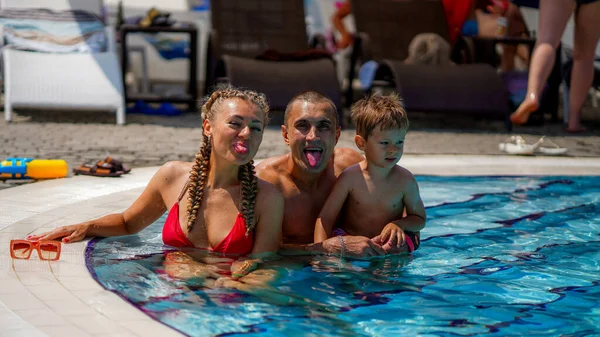 休暇中の家族 水着姿の美しい母 ウォーターパークの運動選手の父と小さな男の子 男と女が冗談で舌を見せる — ストック写真