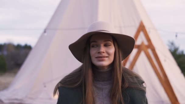 Portret uśmiechnięta kobieta w kapeluszu Stoi w glamping na tle tipi. Zwolnij trochę. Zbliżenie — Wideo stockowe