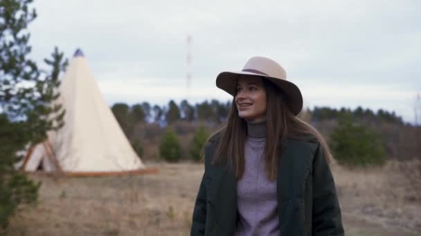 Jonge mooie glimlachende vrouw loopt door het platteland naar glamping buiten tipi. Langzame beweging — Stockvideo