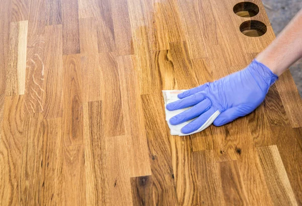 Person working, rubbing oiling with linseed oil natural wooden kitchen countertop before using. Solid wood butcher block countertop maintenance concept.