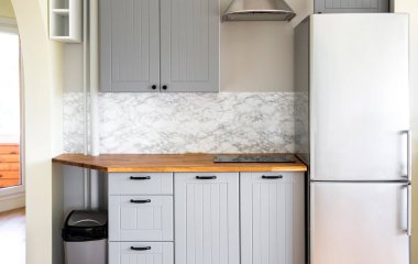 Modern, gri renkli, kendine yapıştırıcı sahte mermer taklit bantlı mutfak. Küçük sobanın içine inşa edilmiş saf, doğal ahşap tezgah..