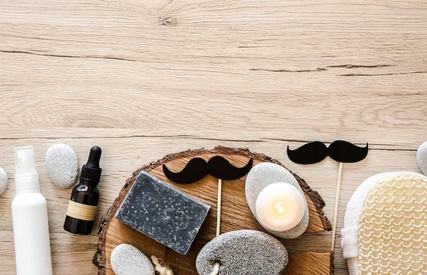 Flat lay composition of various man bathroom products with a lot of copy space. Bar of clay soap, pumice stone, natural bath sponge, moisturizing cream and mustache figurines.