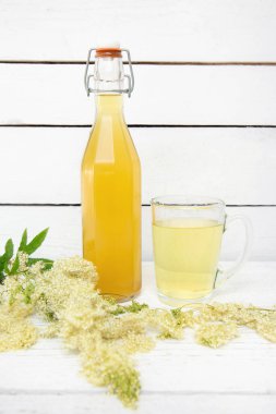 Ev yapımı MeadowSweet Filipendula Ulmaria çiçek şurubu şişesi, bardakta içki ve beyaz renkli ahşap arka planda çayır tatlısı dallar ve çiçekler topladım..
