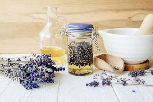 Homemade cold-infused lavender oil. Olive oil covering dried lavender blossoms in a glass jar. A mortar and pestle, with a bundle of lavender flowers for decoration.