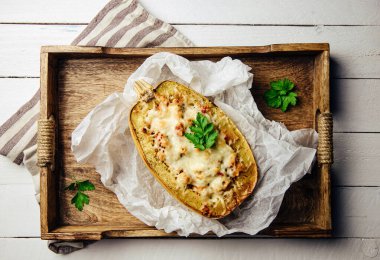 Above view of spaghetti squash or vegetable spaghetti stuffed with minced meat and cheese, served in its shell on wood tray. Homemade dish.