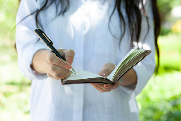 ручка женщины с блокнотом на фоне парка
