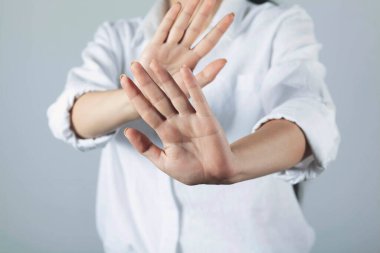 Gri arka planda duran elleri olan genç bir kadın.