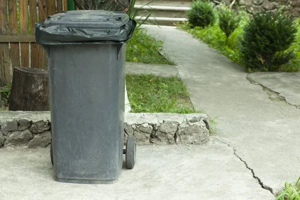 Yellow plastic trash can on the street on the sidewalk in the park. Garbage container outside