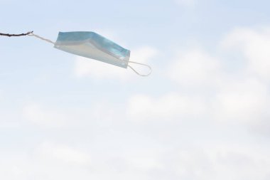 Rüzgar eserken ve gökyüzü arka plan olarak kullanılırken bir ağaç dalına bağlı yüz maskesi.