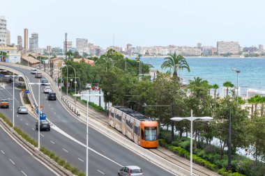 Alicante, İspanya; 8 Temmuz 2020; yollar boyunca uzanan tramvayın manzarası, arabalarla dolu yol, deniz ve arka plandaki binalar açık bir gökyüzü olan yaz günü Pozisyon plajının yanında.