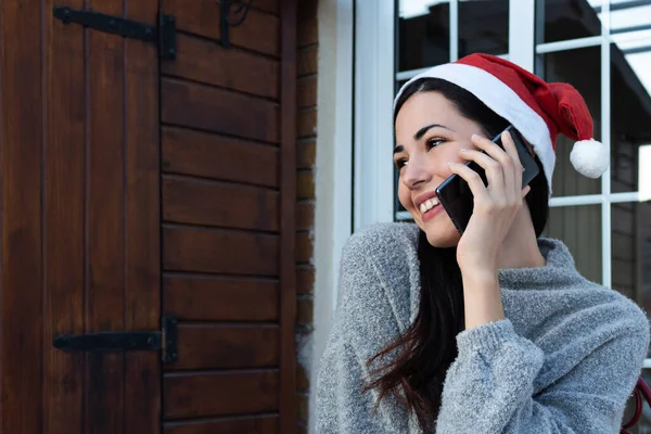 A young woman calling with her cell phone while smiling with a Santa Claus hat on Christmas