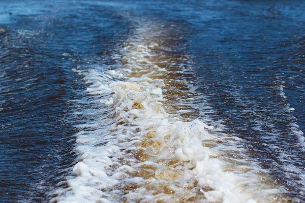 Wake trail with water spray and foam water surface reflecting the blue color of the sky from a speedboat on a summer day