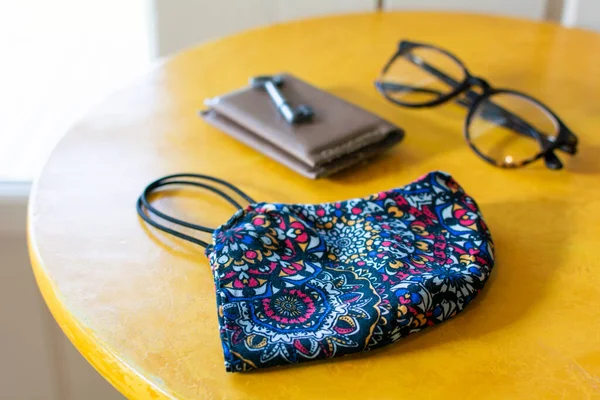 Safety mask, glasses, wallet and key on a yellow table next to the door