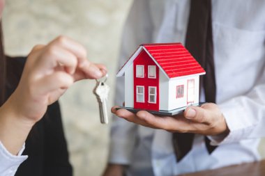Ev satıcısının elinde kırmızı çatı katı ve konseptin anahtarı var. Ürünü alan veya kontrat imzalayan müşteri, ev alıp satma konsepti, ipotek, gayrimenkul