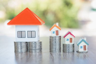 Bir yığın madeni parada turuncu çatı evi ve madeni para basamağında küçük bir ev. Emlak yatırımları için ev ya da kredi almak için para biriktirmek ve tasarruflar sırasında fikir üretmek riskli olabilir..