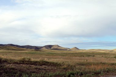 Beyaz bulutlar Sayan Dağları Sibirya Rusya ile mavi gökyüzü altında sarı çim ile geniş bozkır