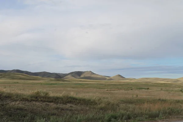 Estepa larga com grama amarela sob um céu azul com nuvens brancas Montanhas Sayan Sibéria Rússia — Fotografia de Stock