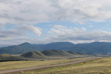 Beyaz bulutlar Sayan Dağları Sibirya Rusya ile mavi gökyüzü altında sarı çim ile geniş bozkır