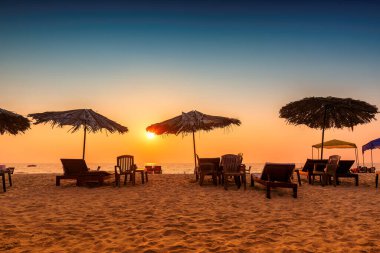 GOA, Hindistan 'da tropik plajda gün batımında şezlonglar ve plaj şemsiyeleriyle.
