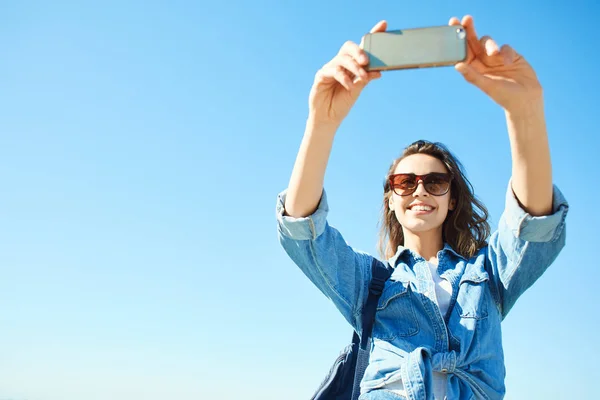 Retrato de una mujer joven y atractiva usando el teléfono en el fondo azul del cielo — Foto de Stock