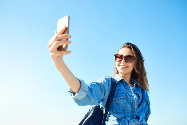 Retrato de una joven atractiva usando un teléfono móvil sobre el fondo azul del cielo — Foto de Stock