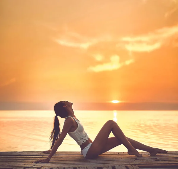 Kaunis seksuaalinen nainen valkoisessa hatussa ja bikinit puulaiturilla merta ja auringonlaskua vastaan — kuvapankkivalokuva
