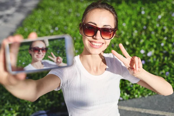 รูปภาพของหญิงสาวที่น่าสนใจ กําลังถ่ายเซลฟี่บนพื้นหลังหญ้าสีเขียว — ภาพถ่ายสต็อก