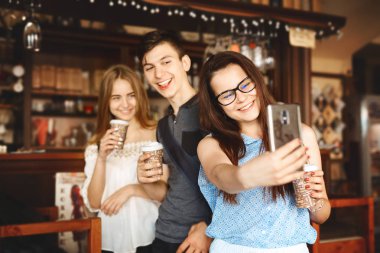 Bir grup arkadaş kafede eğleniyor. Gençler bir kafede buluşuyor. Kâğıt bardaklı genç erkek ve kadınlar kafe tezgahında durup selfie çekiyorlar.