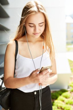 Açık havada kulaklık takan genç sarışın kızın portresi.