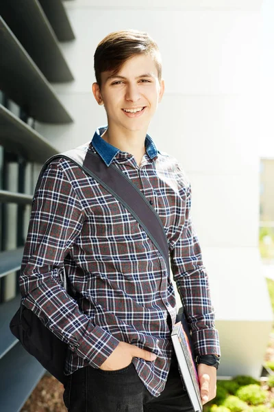 smiling attractive young man student standing and holding notebooks in outdoors