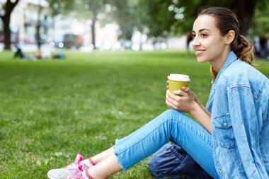 çekici gülümseyen kadın parkta çim caffee bardak kağıt ile oturuyordu