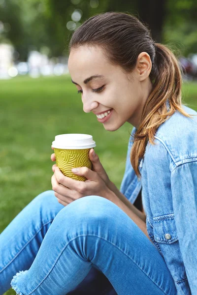 Attraktive Lächelnde Frau Sitzt Mit Pappbecher Kaffee Auf Dem Rasen — Stockfoto