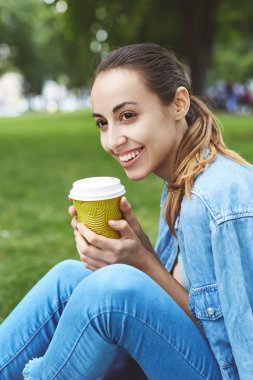 çekici gülümseyen kadın parkta çim caffee bardak kağıt ile oturuyordu