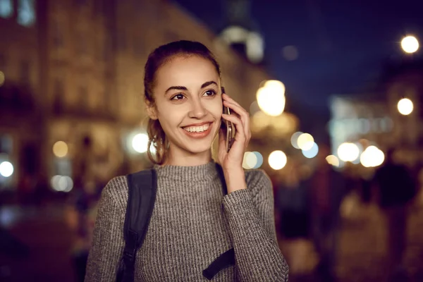 young woman tourist walking on the night street in historic part of city, Ukraine, Lviv. woman smiling and talking by mobile phone