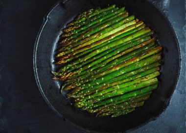 koyu taş arka plan üzerinde Dökme demir tavada yağ ve baharat ile kavrulmuş kuşkonmaz. Vegetfrian ve vegan gıda pişirme. Üst viev